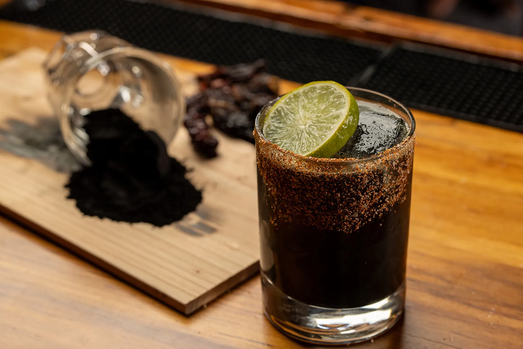 Black cocktail with lime slice and spiced rim.