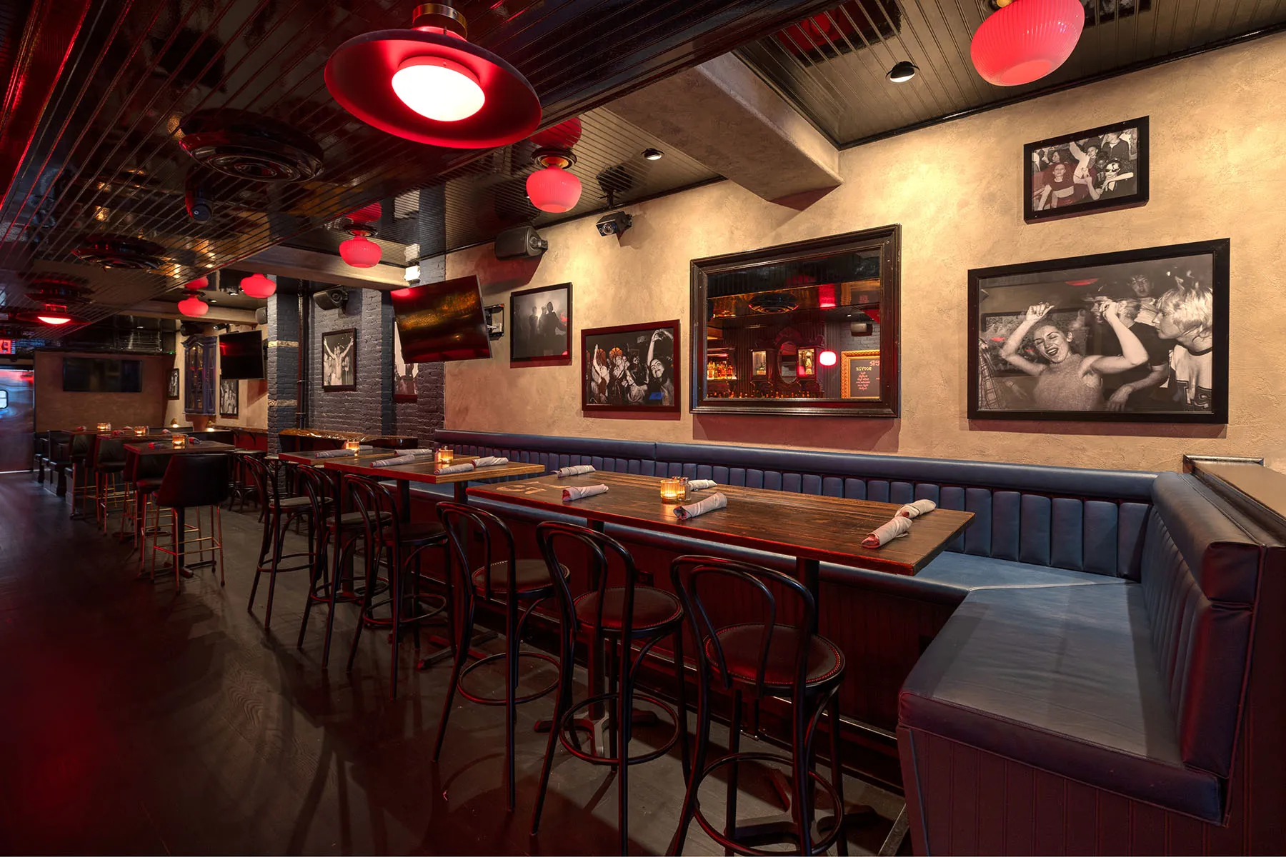 Sports bar with long booth seating, high-top tables, and red hanging lights.
