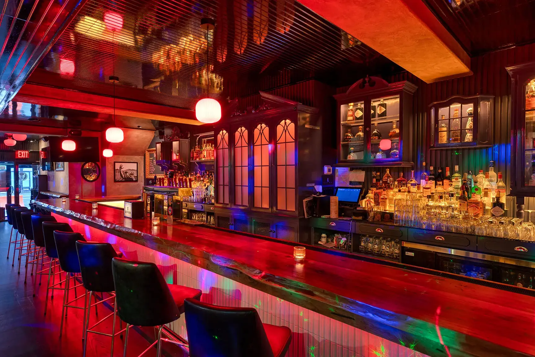 Modern sports bar featuring a glowing red bar counter, black stools, and well-stocked back bar.
