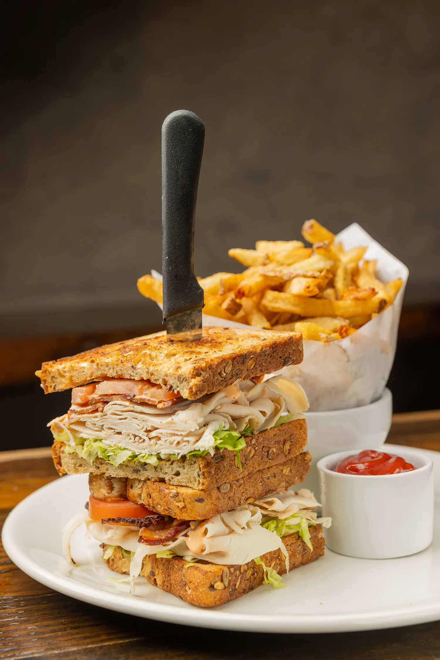 Tall turkey club sandwich stacked with bacon, lettuce, and tomato, served with crispy fries and ketchup.
