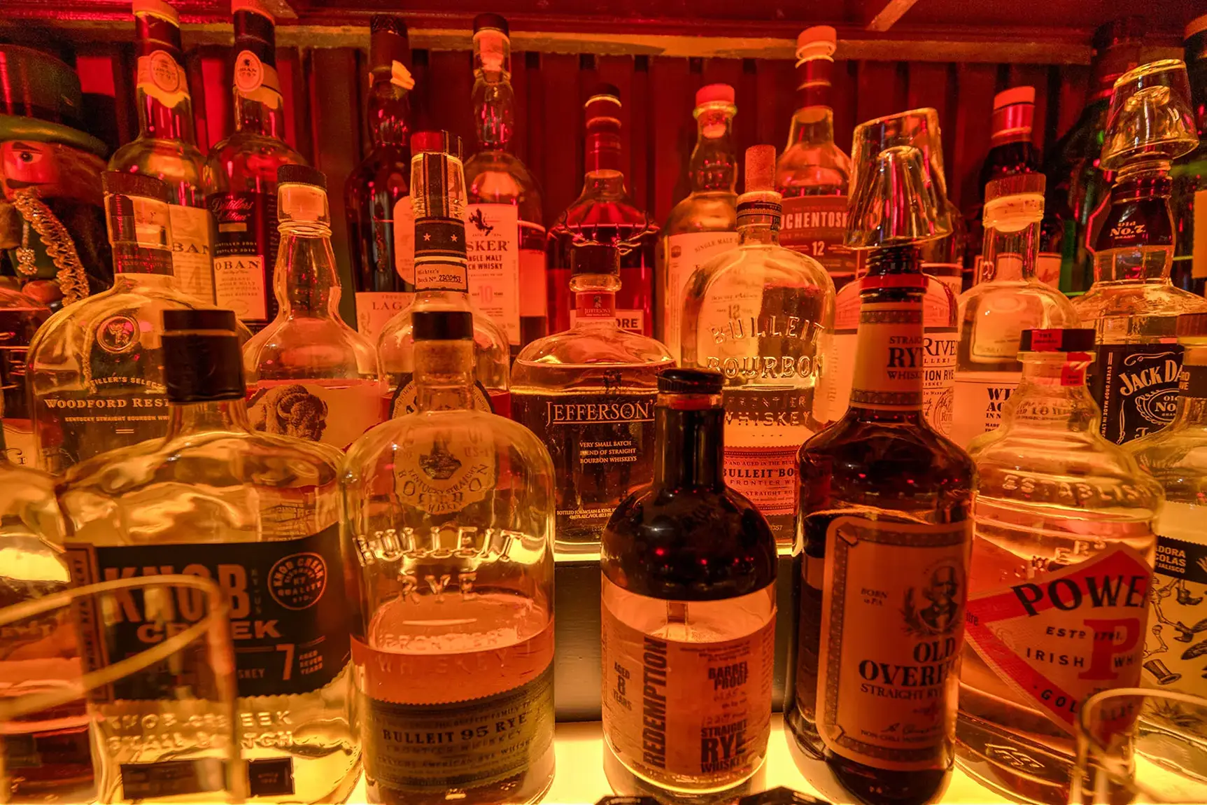 Whiskey and bourbon bottles on a glowing bar shelf.
