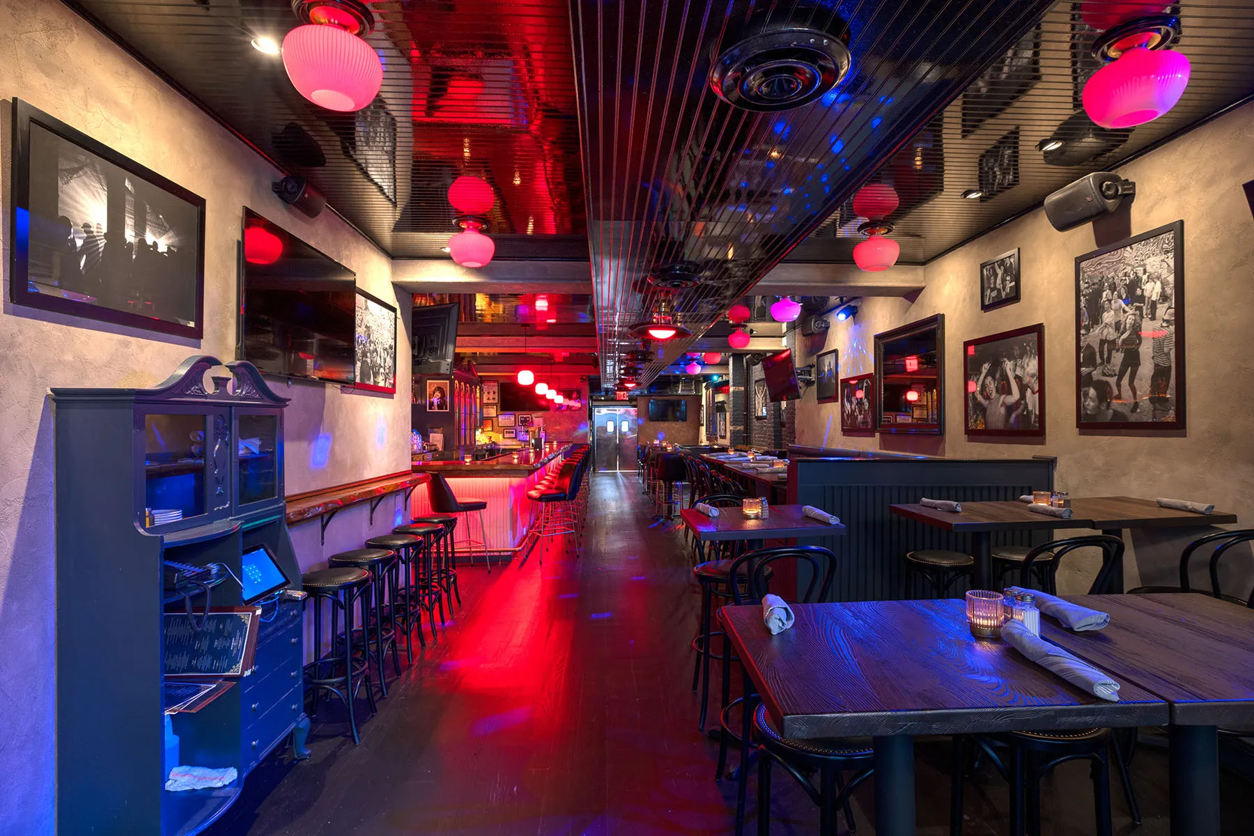 Spacious sports bar with high-top seating, framed photos, and red hanging lights.
