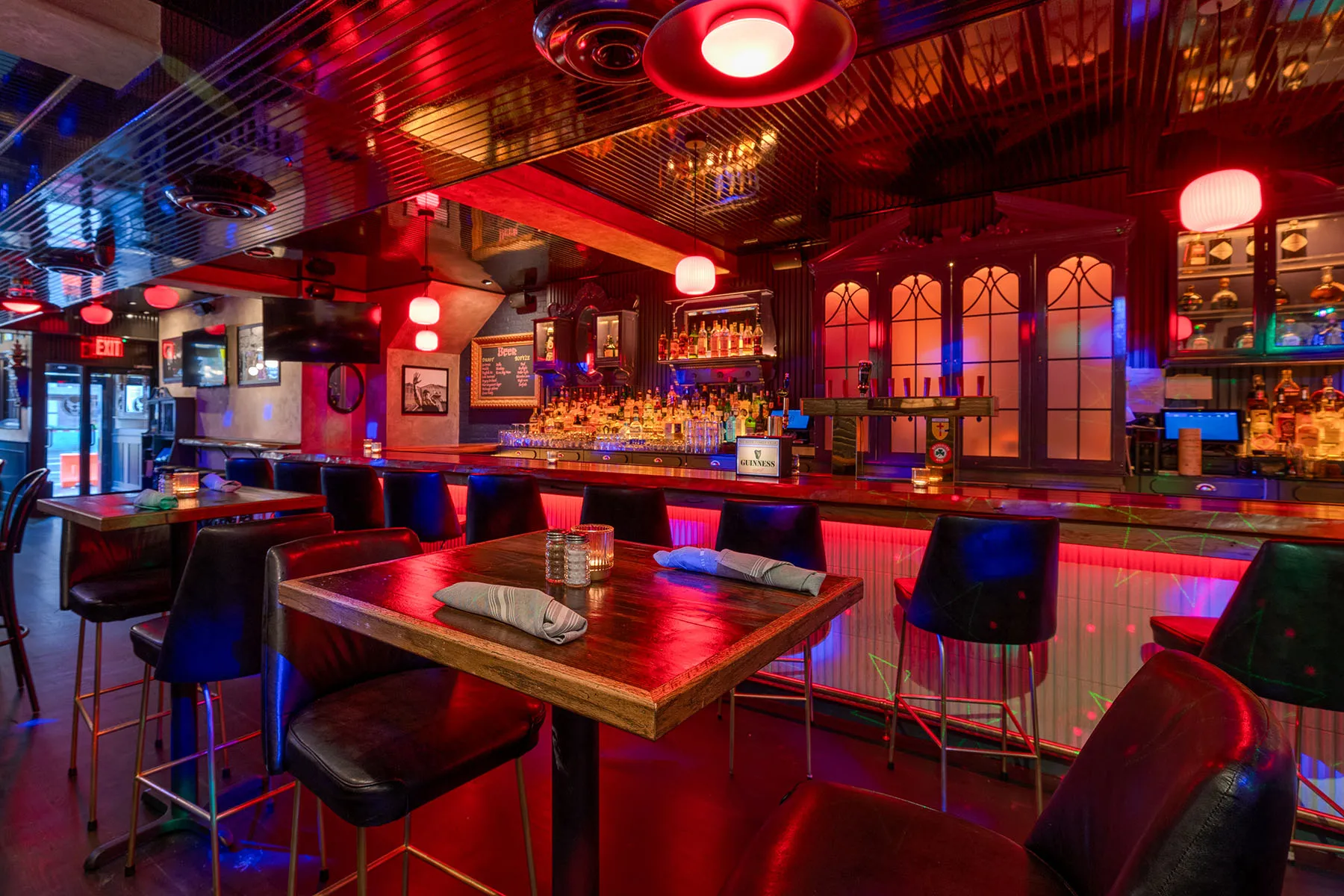 Stylish bar interior with red neon lights, high-top seating, and a well-stocked back bar.
