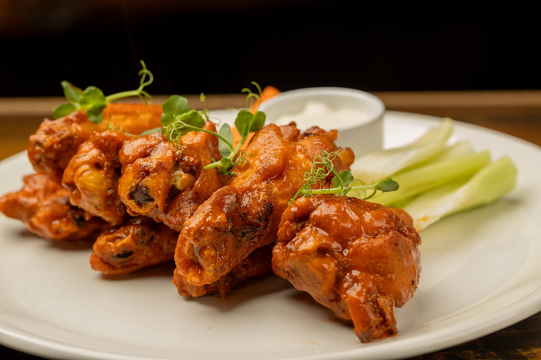 Plate of spicy buffalo wings with celery and dip.
