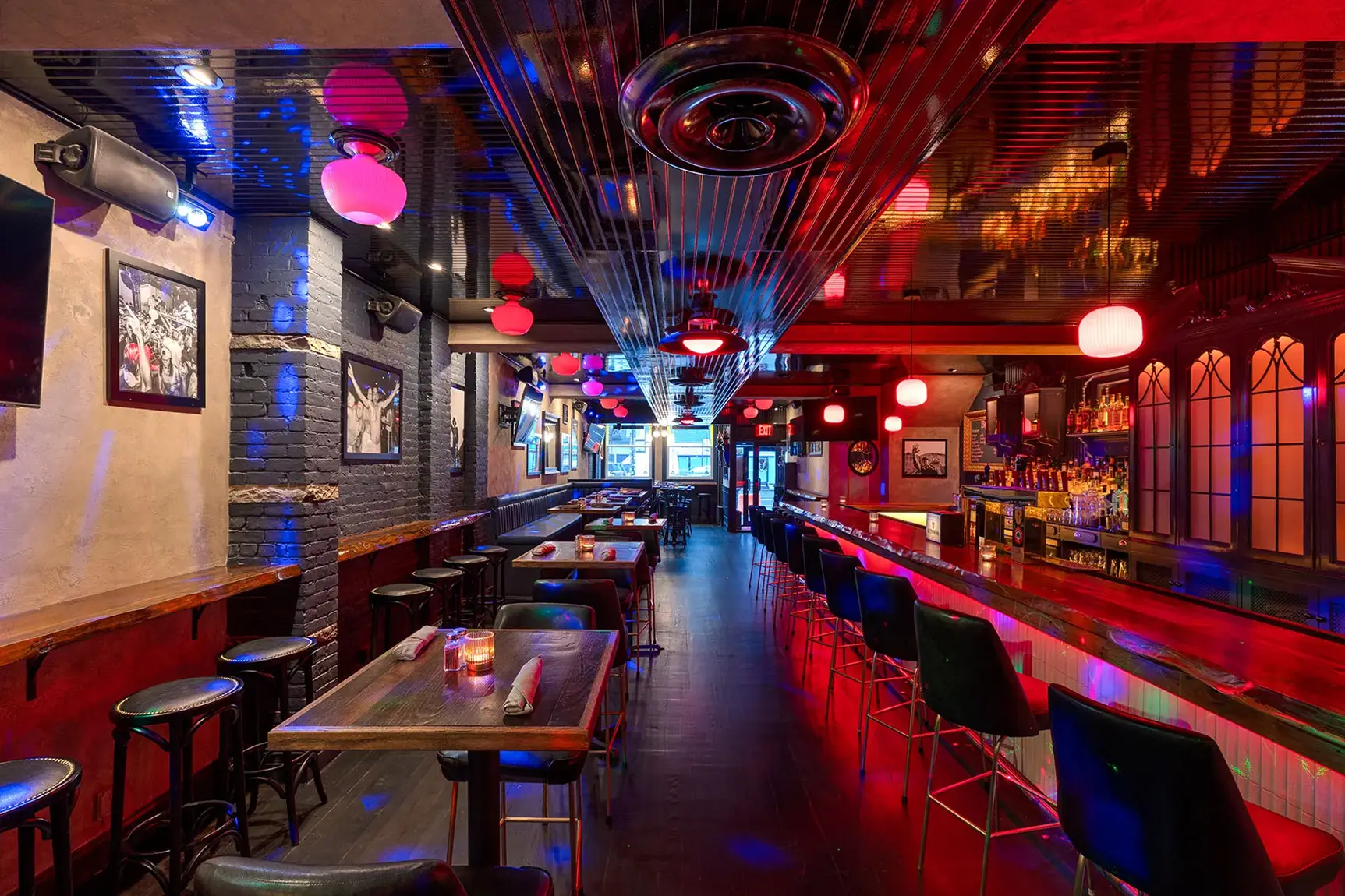 Contemporary bar interior with high-top tables, red lights, and exposed brick walls.
